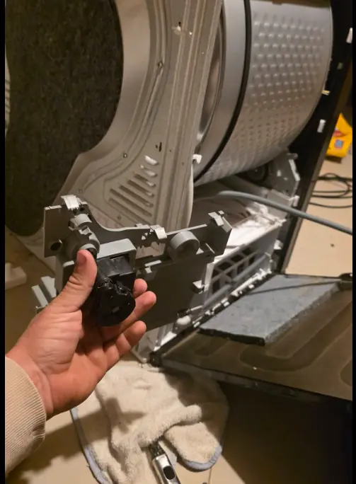 Technician holding a dryer idler pulley next to the open dryer cabinet