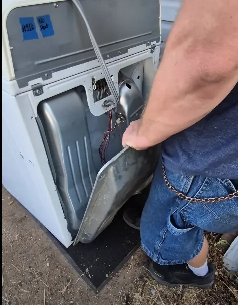 Technician reaching into the back of a dryer to test the thermal fuse